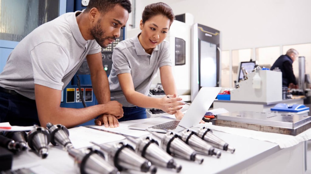 A young woman and a man discussing micro manufacturing processes with semi-assembled precision OEM parts next to them in close-up view