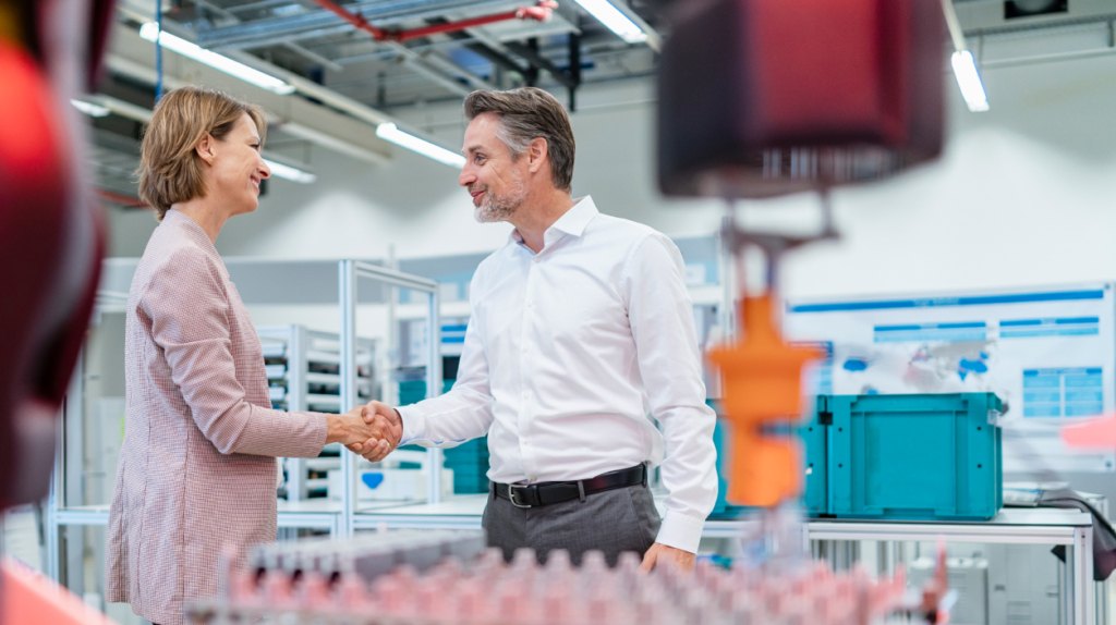 Business professionals shaking hands in a medical device manufacturing plant, emphasizing collaboration and streamlined lead times for clients.